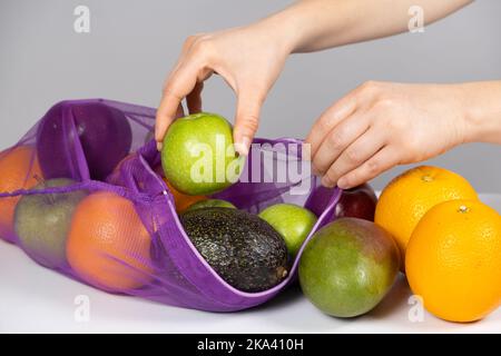 Una donna mette frutto in una rete. Il concetto di abbandonare le borse della spesa in plastica Foto Stock