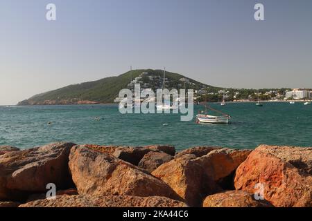 Vista del porto di Santa Eulalia con rocce di difesa del mare in primo piano. Ibiza, Isole Baleari, Spagna. Foto Stock