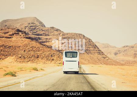 Vista posteriore autobus bianco viaggio su strada asfaltata in montagne panoramiche Wadi rum in Giordania all'aperto portare il turista a destinazione. Turismo cinematografico espresso Foto Stock