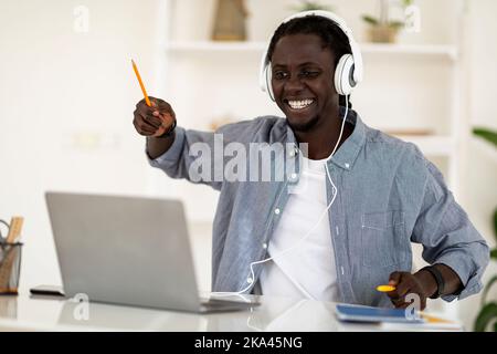 Allegro Black Guy divertirsi mentre si ascolta la musica sul notebook a casa Foto Stock
