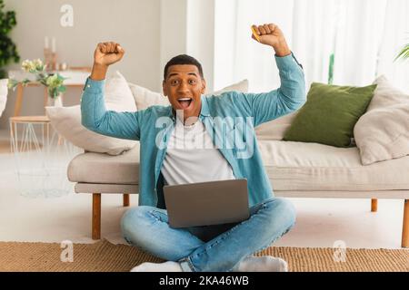 Soddisfatto eccitato uomo afroamericano millenario con bocca aperta alza le mani in su celebrare la vittoria Foto Stock