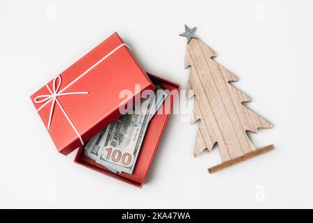 Come spendere, il preventivo di Natale ed il concetto di risparmio. Scatola regalo di natale, pila delle fatture del dollaro e albero di Natale di legno sulla tabella bianca Foto Stock