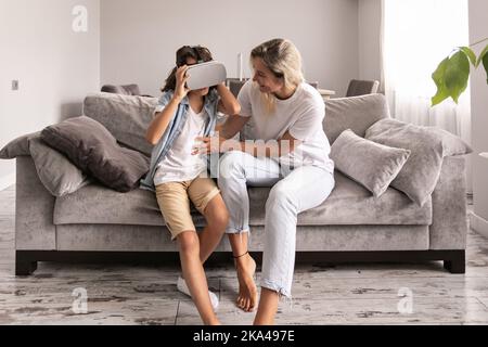 ragazzo che indossa un visore per la realtà virtuale con gli occhiali vr di sua madre nel salotto di casa per divertirsi Foto Stock