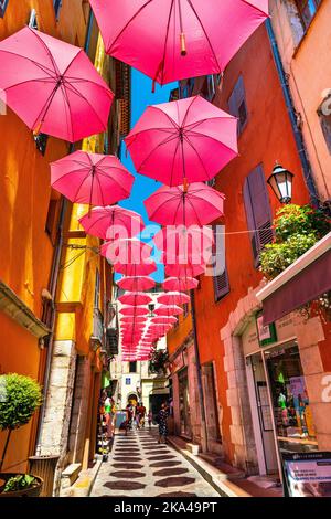 Grasse, Francia - 6 agosto 2022: Case storiche e strade strette decorate con ombrelloni rosa del centro storico della città profumeria Foto Stock