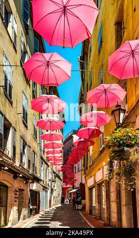 Grasse, Francia - 6 agosto 2022: Case storiche e strade strette decorate con ombrelloni rosa del centro storico della città profumeria Foto Stock