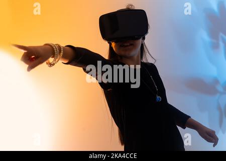 Le ragazze adolescenti si divertono a giocare a metaverse di realtà virtuale con gli occhiali VR, giocare a videogame, guardare film, ascoltare musica, fare shopping. Neon colorato Foto Stock