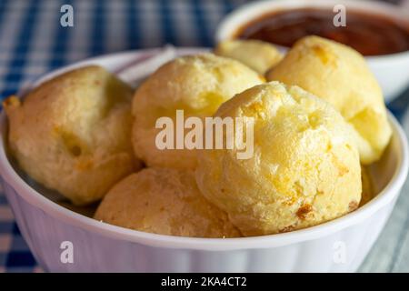 Un primo piano di pane brasiliano al formaggio noto come pao de queijo in una ciotola bianca con ketchup Foto Stock