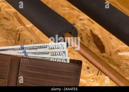 Tubo dell'acqua con isolamento e denaro contante in casa. Protezione antigelo per impianti idraulici, risparmio energetico e concetto di riparazione domestica Foto Stock