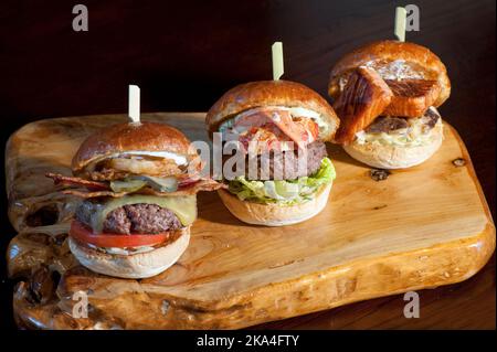 Salmone Burger, aragosta e hamburger di carne e hamburger serviti su un tagliere di legno Foto Stock