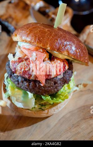 Aragosta e hamburger di carne serviti su un tagliere di legno Foto Stock
