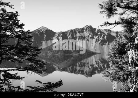 Immagine in bianco e nero della Wizard Tower a Crater Lake, Oregon. L'acqua cristallina crea uno specchio che riflette l'isola e i dintorni. Foto Stock