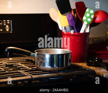 Pentola in acciaio inox su stovetop a gas nero con contenitore rosso contenente spatole Foto Stock