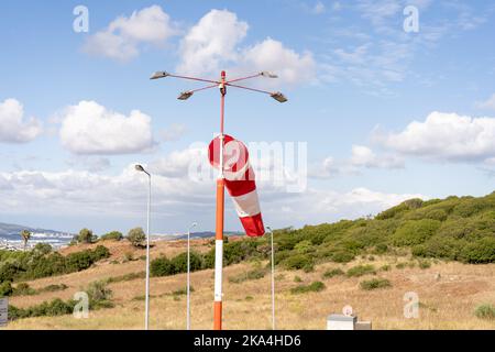 Calza a vento vola. Estate calda giornata in aeroporto sportivo privato con abbandonata windsock, il vento soffia e windsock è pigro movimento. Windsock con cielo nuvoloso montagna e strada con auto sullo sfondo Foto Stock