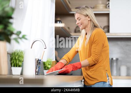 Felice bella donna bionda lavare piatti a casa Foto Stock