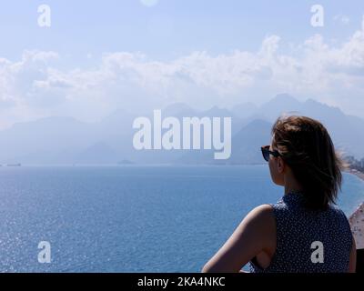 donna in occhiali da sole guarda in lontananza .sfondo del mare e delle montagne Foto Stock