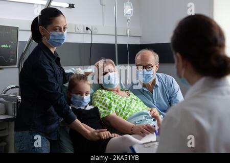 Membro del personale medico della clinica geriatrica che esamina i file delle donne anziane bedridden. Nonna sdraiata nel letto di ospedale che si recupera da infezione da coronavirus, medico che indossa maschere che impediscono la diffusione del virus. Foto Stock