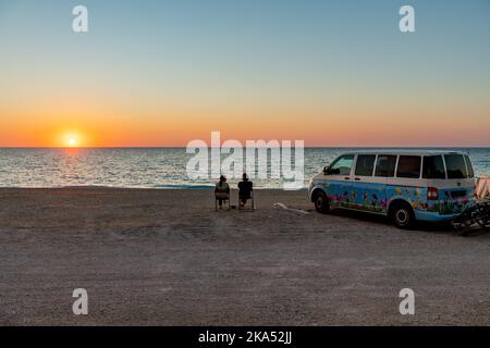 Isola di Lefkada. Grecia-10.17.2022. Un camper parcheggiato su una spiaggia con una coppia che si gode un bicchiere di vino e il tramonto. Foto Stock