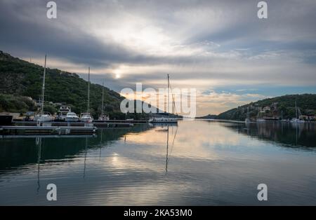 Alba nella baia di Sivota, isola di Lefkada, Grecia con cielo nuvoloso e luce dorata che proietta riflessi sull'acqua calma. Foto Stock