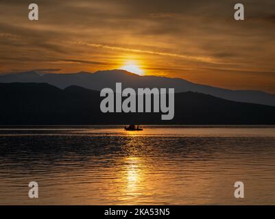 Una piccola pesca in mare catturata dalla luce riflessa del sole che sorge sulla collina. Foto Stock