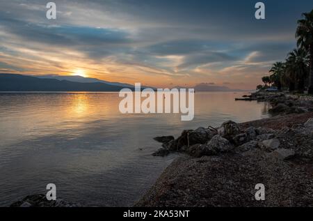 Il sole che sorge sopra la collina che proietta riflessi di luce dorata sul mare calmo. Foto Stock