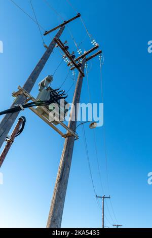 Cavo elettrico sospeso su pali di legno che portano la fornitura di energia elettrica alle aree rurali. Foto Stock
