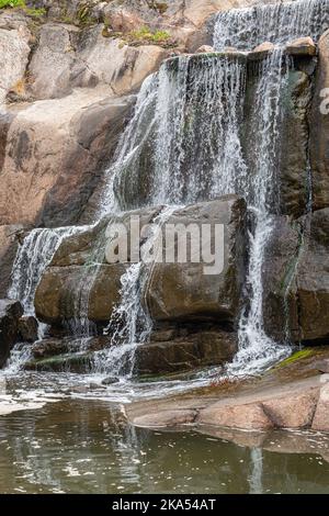 Finlandia, Kotka - 18 luglio 2022: Parco e lago di Sopokanlahti. Primo piano della base della cascata che mostra flussi di acqua bianca su rocce marroni bagnate Foto Stock