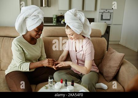 Ritratto di due ragazze con asciugamani che fanno manicure mentre godendo giorno di auto-cura a casa Foto Stock