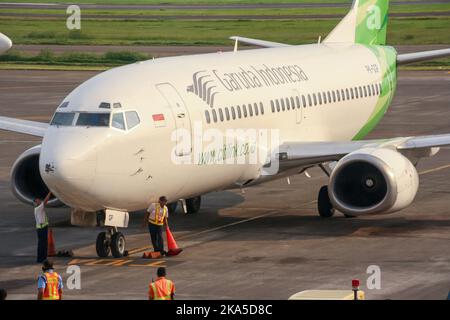 Vista del vettore a basso costo Garuda Indonesia Citilink Airliner sul grembiule con equipaggio a terra all'aeroporto internazionale di Juanda con pista in background. Foto Stock