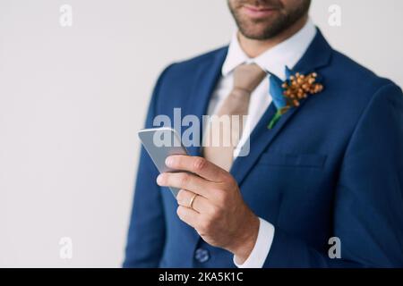 Voti di nozze, in forma mobile. Immagine ritagliata di un elegante sposo utilizzando un telefono cellulare su uno sfondo grigio. Foto Stock