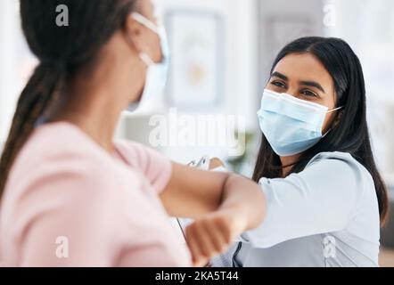 Covid, il gomito e i dipendenti salutano mentre indossano la maschera facciale in ufficio per il lavoro di squadra e la collaborazione. Le donne di affari distensione sociale durante Foto Stock