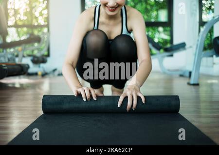 Giovane donna che rotola il suo tappetino nero dopo aver preso una lezione di yoga. Foto Stock