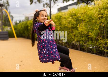 Ragazza sorridente che oscilla su una corda in un parco giochi Foto Stock