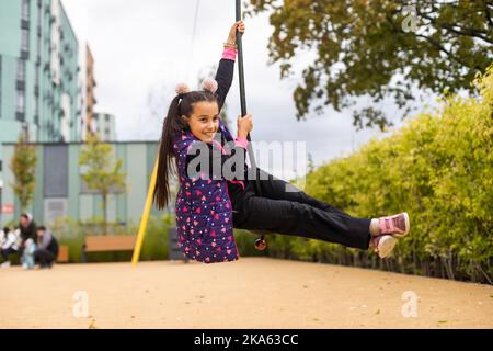 Ragazza sorridente che oscilla su una corda in un parco giochi Foto Stock