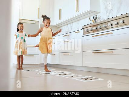 Hopscotch, divertimento e bambini giocare una partita insieme nella cucina della loro moderna casa di famiglia. Felice, sorridere e bambini o sorelle che saltano sopra Foto Stock