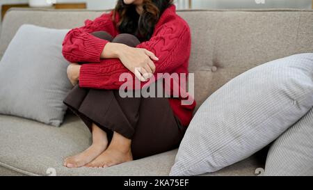 Depressa, triste e stressata giovane donna asiatica seduta sul divano nel suo salotto. Problemi di salute mentale, problemi di relazione. Immagine ritagliata Foto Stock