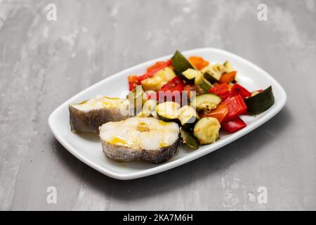 verdure al forno con pesce bollito su piatto bianco Foto Stock