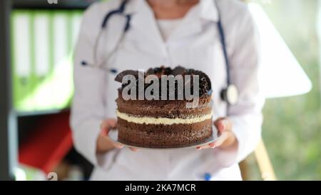 Donna nutrizionista che tiene in mano grande torta al cioccolato Foto Stock