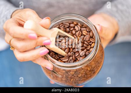 Le mani delle donne che tengono un vaso di vetro pieno di chicchi di caffè. Foto Stock