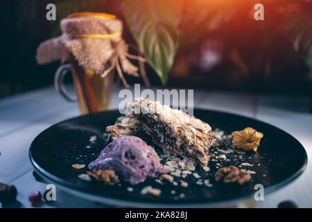 torta napoleone al cioccolato con cucchiaio di gelato alla bacche e tazza da tè nera Foto Stock