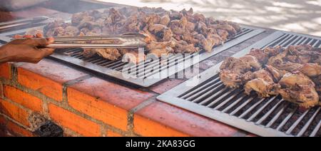 Anonimo afro americano maschio utilizzando pinze per girare ali di pollo sulla griglia durante il barbecue il giorno d'estate Foto Stock