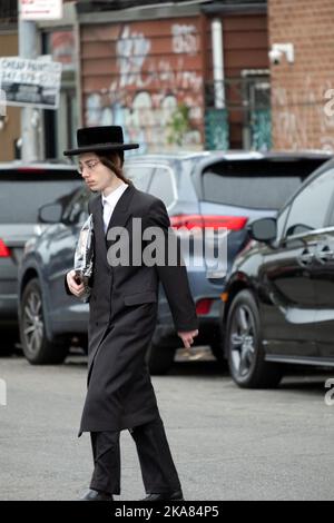 Un giovane ebreo hassidico con lunghi ricci di peyot cammina a casa dopo i servizi mattutini. A Brooklyn, New York. Foto Stock