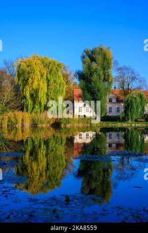 Villaggio stagno con riflessi di alberi colorati in acqua e un vecchio maniero sullo sfondo. Foto Stock
