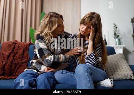 Raccontami i tuoi problemi donna di mezza età che conforta la sua giovane figlia che si siede sul divano Foto Stock