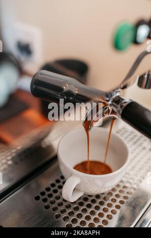 Un primo piano verticale di caffè espresso che viene versato dal filtro nella tazza Foto Stock