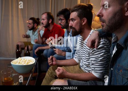 Gruppo di maschi si è concentrato seduto sul divano in un soggiorno guardando una partita di calcio Coppa del mondo. Foto Stock