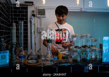 Bangkok, Thailandia. 01 novembre 2022. Un budtender e proprietario di un Happy Hub 420, un piccolo dispensario di cannabis a Bangkok, mostra il suo prodotto insieme a una collezione di bong di vetro. Un budista e proprietario di un piccolo dispensario di cannabis di proprietà locale a Bangkok mostra il suo prodotto insieme a una collezione di bong di vetro. La Thailandia ha depenalizzato la marijuana nel giugno 2022, portando a una corsa verde con varie complicazioni legali e politiche che attualmente si stanno facendo strada attraverso il processo legislativo della Thailandia. Matt Hunt./ Neato Foto Stock