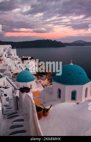 Una splendida foto verticale del villaggio di Oia a Santorini, in Grecia sotto le nuvole rosa al tramonto Foto Stock