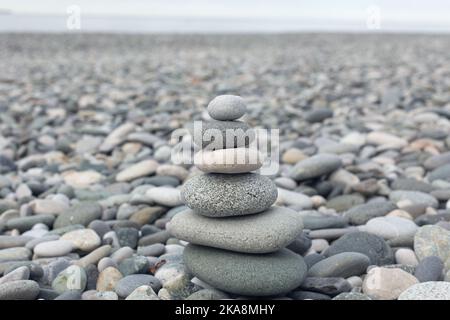 Pietra Cairn su sfondo grigio Pebble Sea. Scultura Rock Zen Foto Stock