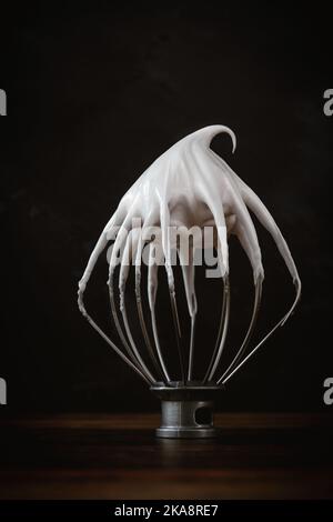 Primo piano verticale una frusta impastatrice ricoperta di crema su una superficie di legno Foto Stock