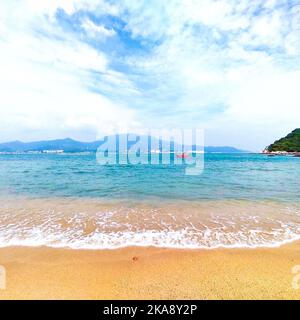 Una splendida vista sulle morbide onde dell'acqua di mare blu su una spiaggia di sabbia con le montagne sullo sfondo Foto Stock